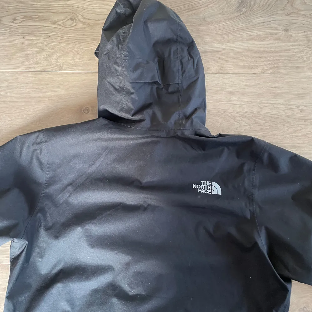 Säljer en svart regnjacka från The North Face med huva och dragkedja. Jackan har en stilren design och är perfekt för regniga dagar. Den är tillverkad i ett slitstarkt material och har The North Face-loggan på bröstet och ryggen.. Takit.
