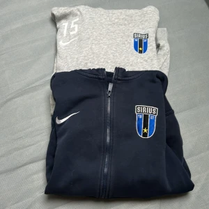 Nike Sirius hoodie i grått och blått - Säljer två hoodies från Nike med Sirius-logga. En är grå med nummer 15 tryckt på bröstet och en är mörkblå. Båda har dragkedja och huva, samt Nike-logga på bröstet. Perfekt för sportiga tillfällen eller som en casual look. Bra använt skick den mörkblå syns i färgen att den är tvättad några ggr