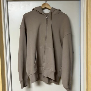 Beige hoodie med dragkedja Oversized - Säljer en stilren beige hoodie med dragkedja och luva. Tröjan har en avslappnad passform med långa ärmar och praktiska fickor framtill. Perfekt för en casual look.