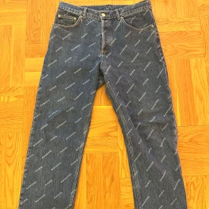 Blå jeansbyxor från Sandro Paris - Snygga blå jeansbyxor från Sandro Paris med ett diskret mönster av märkets namn över hela tyget. Byxorna har en klassisk femficksdesign och knappgylf. Perfekta för en stilren look. Nypris 1900kr. Storlek: 32/32 skick: som nya endast tvättade en gång. Passformen är straight och dem lägger sig bra över skorna.