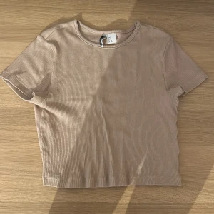 Beige ribbad topp från H&M - Säljer en beige ribbad topp från H&M. Den har en rund halsringning och korta ärmar. Perfekt för en avslappnad stil.