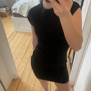 Svart kortklänning - Snygg svart kortklänning med en tight passform och korta ärmar. Perfekt för en stilren look. Klänningen är enkel och elegant, vilket gör den lätt att matcha med olika accessoarer. Helt oanvänd och ny med prislapp