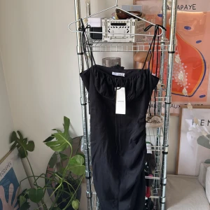 Svart klänning från Adoore (Santorini dress) - Elegant svart klänning från Adoore med smala axelband och en knytning framtill. Helt oanvänd.