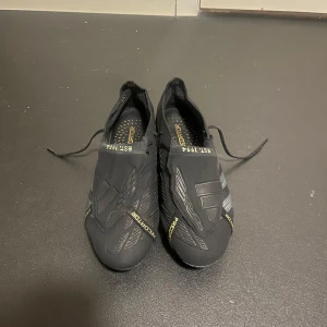 Svarta Adidas Predator fotbollsskor - Säljer ett par svarta Adidas Predator fotbollsskor med snygga guldiga detaljer. Skorna har en strömlinjeformad design med snörning och är perfekta för fotbollsplanen. De har en robust sula med dobbar för optimalt grepp. Knappast använda, ca 5-7 gånger. Pris kan diskuteras vid snabb affär.