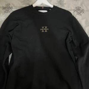 Svart sweatshirt från Les Deux - Snygg svart sweatshirt från Les Deux med deras logga i guld på bröstet. Tröjan har en klassisk rund hals och långa ärmar. Perfekt för en stilren och avslappnad look. Pris kan diskuteras!!