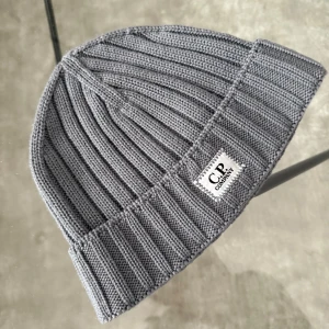 C.P. Company mössa - Snygg grå ribbad mössa från C.P. Company. Tillverkad i mjukt extra fint merinoull med en stilren design och logotyp framtill. Perfekt för kyliga dagar. Köptes ny för 100€ motsvarar 1150kr