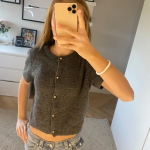 Grå kofta från H&M - Säljer en stilren grå kofta från H&M med knappar framtill. Koftan är tillverkad i en mjuk blandning av polyester, akryl och ull, vilket gör den både bekväm och varm. Perfekt för lager-på-lager under kyligare dagar🩵