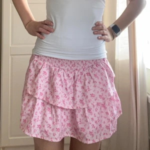  kjol med volang - Söt rosa kjol med blommigt mönster och volangdetaljer. Perfekt för en somrig look. Den har en elastisk midja för bekväm passform. 🩷