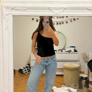 Svart  topp/ linne  - Säljer en stilren svart  topp/ linne. Perfekt för en kväll ute eller en avslappnad dag. Toppen är tight och smickrande, vilket gör den till ett mångsidigt plagg i garderoben. Har bara ett band och enda sidan är bandlös 