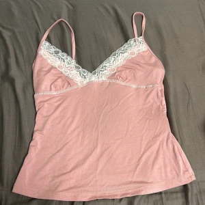 Rosa linnetopp med spetsdetaljer - Söt rosa linnetopp med smala axelband och v-ringning dekorerad med vit spets. Perfekt för varma dagar eller som ett lager under en tröja. Säljs för att jag inte använder den. 