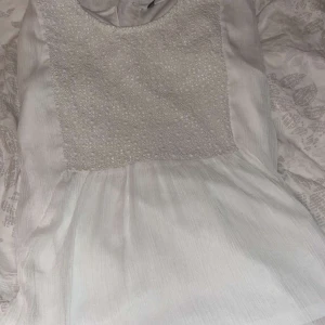 Vit blus med spetsdetaljer - Säljer en söt vit blus med spetsdetaljer på bröstet. Blusen har korta ärmar och en luftig passform, perfekt för varmare dagar. Den är gjord i ett lätt och bekvämt material som ger en avslappnad look.