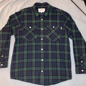 Carhartt WIP Flanellskjorta/Overshirt - Säljer en snygg grön och blå rutig skjorta från Carhartt. Skjortan har långa ärmar och knappar framtill samt två bröstfickor med knappstängning. Perfekt för en avslappnad stil. Använd men i mycket bra skick!