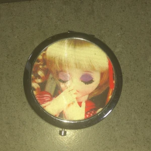 Liten spegel med docka på💗 - Säljer en söt rund spegel med en docka på🫶är i en silverfärgad ram och är perfekt att ha i väskan💗💗 stänger och öppnat även ögonen när man typ vänder på den