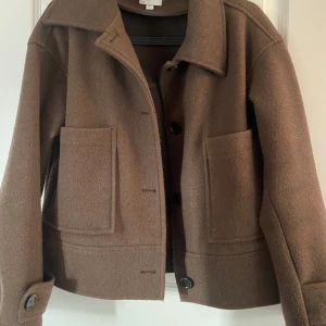 Brun ulljacka från Kappahl - Säljer en snygg brun ulljacka från Kappahl i storlek S. Jackan har en klassisk design med stora fickor och knappar framtill. Perfekt för höst och vår, den är både stilren och varm. Passar till alla tillfällen! 🍂