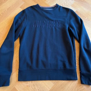Mörkblå tröja från Hilfiger  - Säljer en snygg mörkblå tröja från Hilfiger. Den har en diskret logga på bröstet och är perfekt för både vardag och lite finare tillfällen. Tröjan är i bra skick och har långa ärmar. Passar perfekt till höst och vinter!