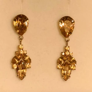 Söta drop örhängen  - Gulliga örhängen i ljust varm brun nyans på kristallerna - jätte fina till hösten :) guldfärgad metall  Vet ej märket, skicket är använt men fint  Inte något exklusiva tror jag utan kommer nog från någon klädkedja eller glitter eller nåt :)