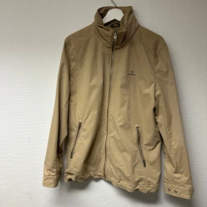 Beige jacka från GANT NY - Säljer en snygg beige jacka från GANT i storlek S. Jackan har en dragkedja framtill och två praktiska fickor med dragkedjor. Perfekt för höst och vår, med en stilren design som passar till det mesta. 🧥Använd 1-2 gånger bara och är fortfarande i nyskick!