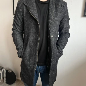 Grå kappa från Zara Man - Säljer en stilren grå kappa från Zara Man i storlek S. Den har en klassisk design med diskret mönster och långa ärmar. Perfekt för höst och vår, med en snygg passform som funkar både till vardags och fest. Tillverkad i Portugal.