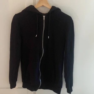 Svart hoodie från ASOS Design - Säljer en svart zip hoodie från ASOS Design i storlek XS. Den har en dragkedja framtill och en mysig huva med snören. Perfekt för höst och vinter, och passar till både vardag och chill. Skön och stilren, ett måste i garderoben! 🖤