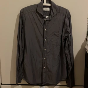 Grå skjorta från Eton - Säljer en stilren Slim-fit grå skjorta från Eton i storlek 38 (S) Skjortan har en slim passform och är tillverkad i ett lätt och bekvämt material. Den har långa ärmar och knappar framtill, samt en praktisk bröstficka. Perfekt för både vardag och fest! 🕺