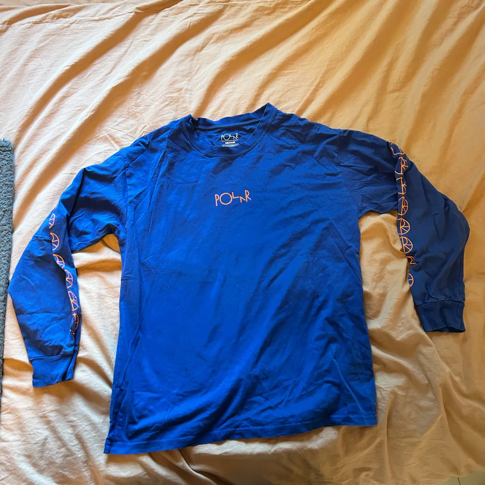 Säljer en blå långärmad tröja från Polar Skate Co. med orangea tryck längs ärmarna och logga på bröstet. Tröjan är i bomull och har en normal passform. Skön och stilren för alla tillfällen! . T-paidat.
