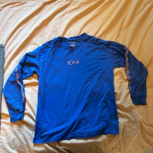 Blå långärmad tröja från Polar Skate Co. - Säljer en blå långärmad tröja från Polar Skate Co. med orangea tryck längs ärmarna och logga på bröstet. Tröjan är i bomull och har en normal passform. Skön och stilren för alla tillfällen! 