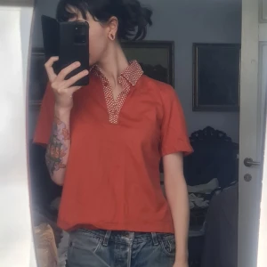 Polo/pikétröja orange S/M - Kanske hemsydd (köpt second hand). Fint skick. Känns som 100% bomull. Bröstvidd: 49 Nederkant: 50 Längd: 55