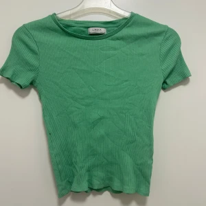 Grön t-shirt  - En längre t-shirt/topp med en grönaktig färg. Den är väldigt fin och färgen gör den mer unik. Den kommer inte till användning.