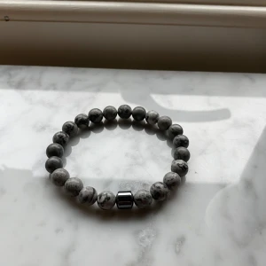 Grått pärlarmband med metallisk detalj - Snyggt grått pärlarmband med marmorerade stenar och en cool metallisk kubdetalj. Perfekt för att ge din outfit en stilren touch. Armbandet är elastiskt och passar de flesta handleder. Perfekt accessoar för både vardag och fest! Ändå är använd ett fåtal gånger 