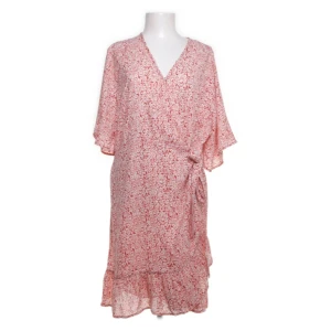 Rosa blommig klänning - Säljer en superfin rosa blommig klänning med v-ringning och volangdetaljer. Den har en omlottstil och trekvartsärmar, perfekt för vår och sommar. Klänningen är i ett lätt och luftigt material, vilket gör den idealisk för varma dagar.
