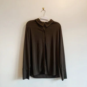 Svart långärmad skjorta från H&M - Snygg svart långärmad skjorta från H&M med klassisk krage och knappar framtill. Perfekt för en stilren look. Tillverkad i ett mjukt och bekvämt material.