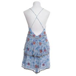 Blommig blå klänning från Zara - Säljer en söt blå klänning från Zara med blommigt mönster och tunna axelband. Klänningen har en omlott-design med volangdetaljer och en öppen rygg. Perfekt för sommarens varma dagar!