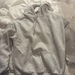 Grå hoodie från BikBok - Säljer en stilren grå hoodie från BikBok i storlek XS. Den har en klassisk design med känguruficka och justerbar huva med dragsko. Perfekt för en avslappnad look.