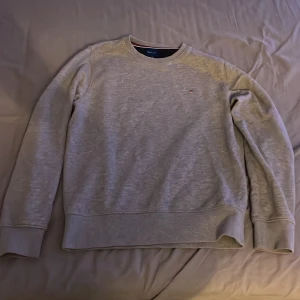Grå sweatshirt från GANT - Säljer en stilren grå sweatshirt från GANT med broderad logga på bröstet. Tröjan har långa ärmar och en klassisk rund halsringning. Perfekt för en avslappnad look.