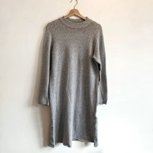 Grå stickad klänning från Jacqueline de Yong - Mysig grå stickad klänning från Jacqueline de Yong. Perfekt för kyligare dagar med sin långa ärm och bekväma passform. Tillverkad i en mjuk polyesterblandning som ger en skön känsla mot huden. Enkelt och stilrent plagg som passar till många tillfällen.