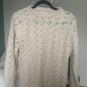 Beige stickad tröja  - Säljer en beige stickad tröja från Hailys med ett fint hålmönster. Tröjan har långa ärmar och en rund halsringning. Perfekt för kyliga dagar!