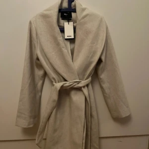 Off white vinter kappa från Bik Bok - Säljer en super fin vinter kappa. Kappan har en elegant knytning i midjan och långa ärmar. Perfekt för att hålla sig varm och snygg under kyliga dagar. 🧥✨pris går självklart att diskutera 