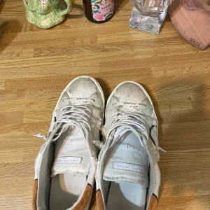 Vita sneakers från Philippe Model - Snygga vita sneakers från Philippe Model med slitna detaljer och bruna hälflikar. Skorna har snörning och en robust sula. Perfekta för en avslappnad stil. Obs slitningarna är design, hör av er vid minsta fundering, priset ej hugget i sten 