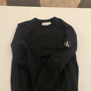 Svart tröja från Calvin Klein Jeans - Säljer en stilren svart tröja från Calvin Klein Jeans med CK-logga på ärmen. Vädligt fräsch tröja för priset! Ny pris 1099kr