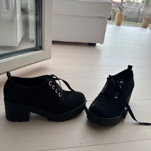 Svarta skor med klack och snörning - Snygga svarta skor med klack och snörning, perfekta för en stilren look. Skorna har en robust sula och är tillverkade i ett material som ger en elegant finish.