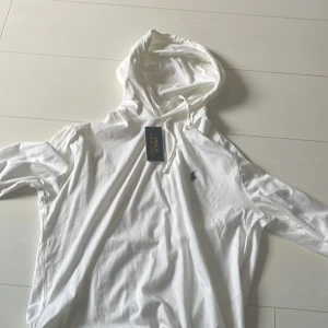 Vit hoodie från Ralph Lauren - Säljer en stilren vit hoodie från Ralph Lauren med den klassiska loggan broderad på bröstet. Tröjan har ett  tunnare material, helt ny