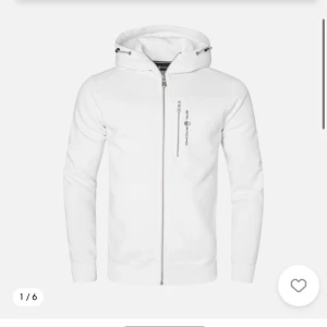 Vit huvtröja med dragkedja - Snygg vit huvtröja med dragkedja och justerbar huva. Perfekt för en stilren och avslappnad look. Tröjan har en praktisk bröstficka med dragkedja och ribbade muddar vid ärmslut och nederkant.