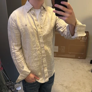 Beige linneskjorta från Morris - Säljer en stilren beige skjorta från Morris i linne. Skjortan har långa ärmar och knappar framtill. Perfekt för en avslappnad men ändå elegant look. Perfekt inför sommaren. Nypris på denna är ca 1700kr. Skriv vid funderingar!