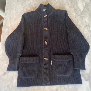 Mörkblå stickad cardigan  - Skick: 7,5/10. Knappen längst ner är lite svår att stänga annars finns det inga defekter. Tröjan är väldigt tjock och är gjord av 100% ull. Från märket saint James som är baserat i Frankrike. Om du är osäker på om den kommer passa kan du alltid fråga om måtten!