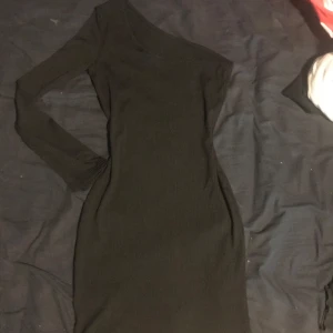 Svart oneshoulder klänning - Snygg svart oneshoulder klänning med lång ärm. Perfekt för en stilren och elegant look. Klänningen har en tight passform som framhäver figuren.