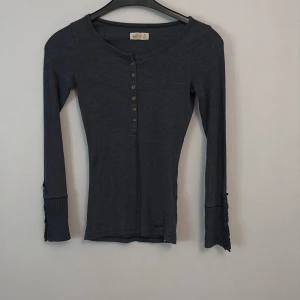 Mörkgrå ribbad tröja från Hollister - Säljer en mörkgrå ribbad tröja från Hollister i storlek XS. Tröjan har långa ärmar och knappar framtill, vilket ger en stilren look. 