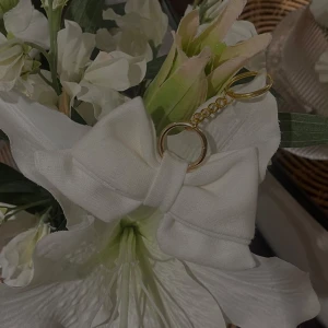 Vit rosett nyckelring/bagcharm - Charmig vit rosett nyckelring med guldfärgad/silverfärgad kedja och ring. Perfekt som accessoar för att ge en söt touch till väskan eller nycklarna. (Vi erbjuder även att mötas upp i söder, huddinge, tyresö, lidingö.)