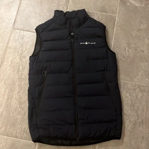 Marinblå  dunväst från Sail Racing - Snygg marinblå dunväst från Sail Racing med dragkedja och logotyp på bröstet. Västen är har två praktiska fickor med dragkedja. Perfekt för kyligare dagar. Storleken är för 14-16 år. Kan gå ner i pris vid snabb affär. Hör av er vid frågor mvh Colin☺️