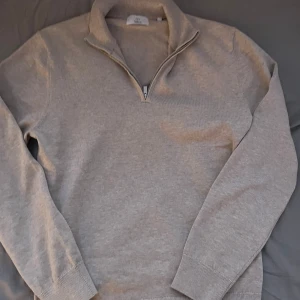 Half zip tröja  - Säljer en stilren beige tröja från Bläck med dragkedja vid halsen. Tröjan har långa ärmar och en ribbad krage. Perfekt för en avslappnad och snygg look. Helt ny
