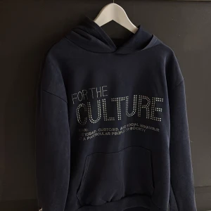 Svart hoodie med textdetaljer - Snygg svart hoodie med texten 'FOR THE CULTURE' i fram och 'REAL ARTISTIC PEOPLE' på baksidan. Hoodien har en klassisk design med känguruficka och en broderad logga på ärmen. Perfekt för en avslappnad stil, prövad 1 gång sen dess 0💕 kan även passa för storlek M💕